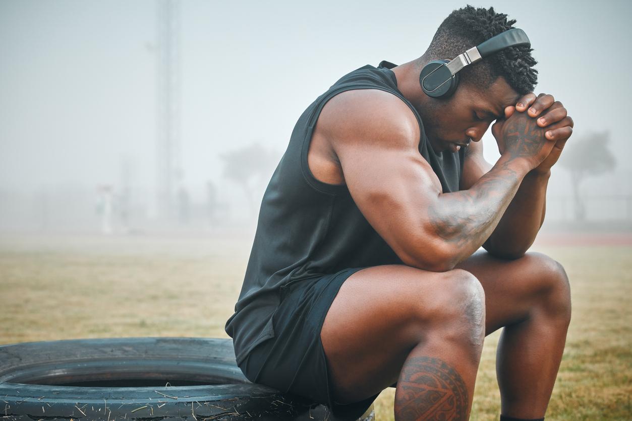 Strong man in tank top and shorts takes a break from workout to think 