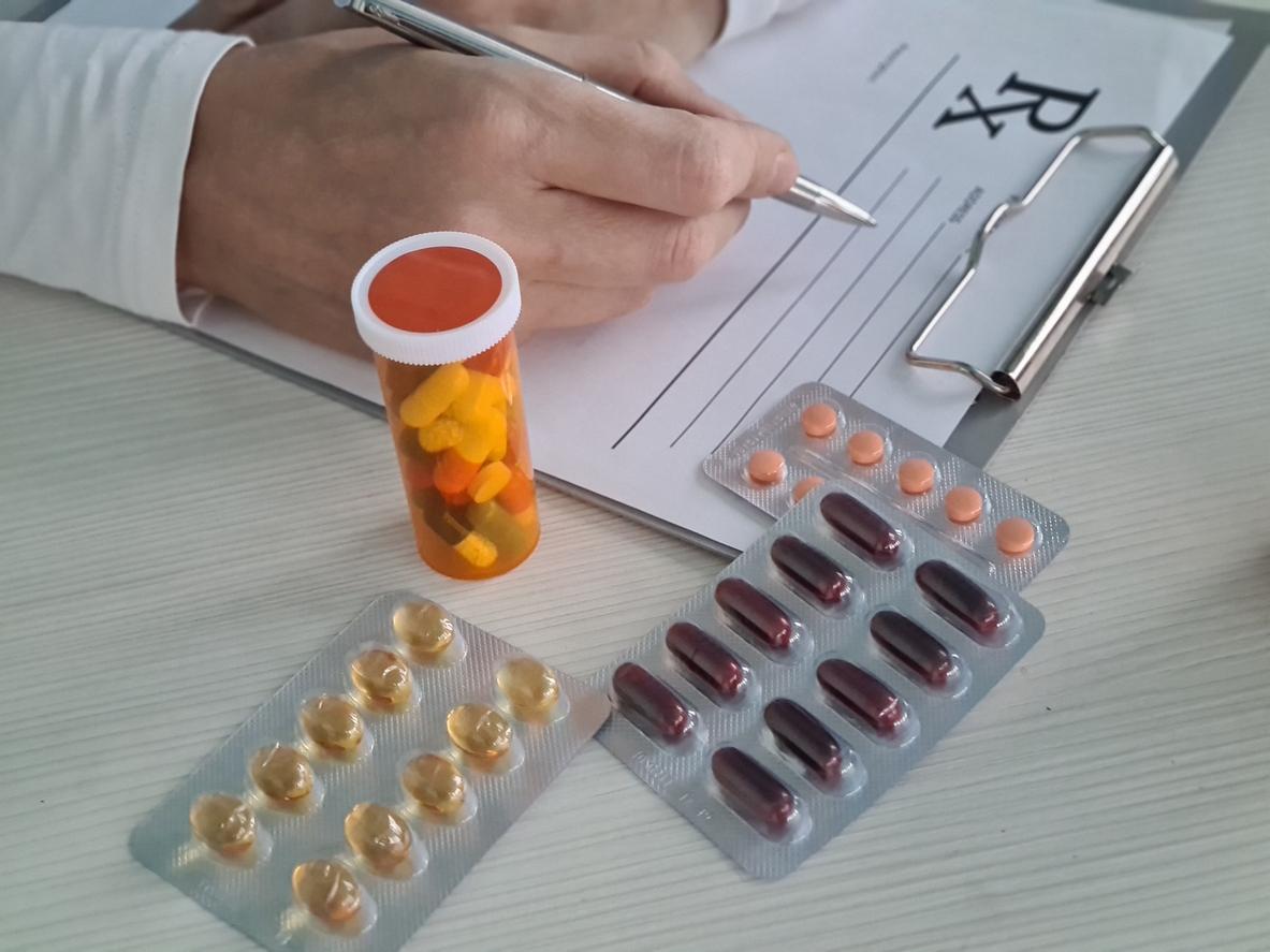 Doctor writing prescription for medication with pills and capsules on desk